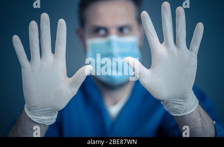 Éclosion de COVID-19. Aide à arrêter la propagation du virus. Homme médecin ou infirmière portant un masque chirurgical pour le visage et des gants EPI montrant les mains en MOUVEMENT D'ARRÊT. Reste s. Banque D'Images