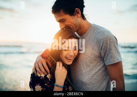 Homme embrassant sa petite amie tenant une rose à la plage. Couple à leur première date à la plage. Banque D'Images