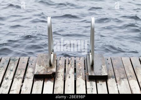 Bord de jetée en bois avec rails métalliques pour nager sur une côte de lac encore Banque D'Images