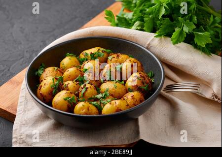 Jeera Aloo dans un bol noir sur fond d'ardoise sombre. Jeera Aloo est un plat de cuisine indienne avec des pommes de terre pour bébé, des graines de jeera et de la coriandre. Banque D'Images