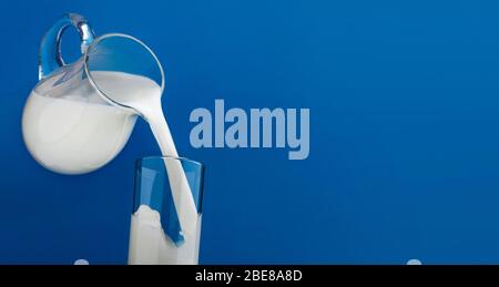 Verser du lait dans le verre isolé sur fond bleu Banque D'Images