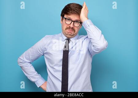 Triste Manager européen malheureuse avec moustache déchu et bouleversée, se tenant sur fond bleu, exprimant tristesse et émotions négatives Banque D'Images