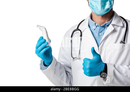 vue rognée du médecin dans le masque médical et le manteau blanc tenant le pyromètre sans contact et montrant le pouce isolé sur blanc Banque D'Images