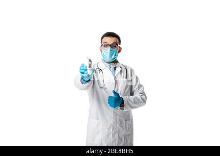 médecin dans le masque médical et manteau blanc tenant pyromètre et montrant pouce isolé sur blanc Banque D'Images