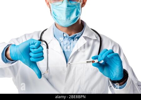 vue rognée du médecin dans le masque médical et le manteau blanc tenant le thermomètre numérique et montrant le pouce vers le bas isolé sur blanc Banque D'Images