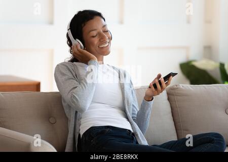 Une femme noire heureuse écoute de la musique sur un casque Banque D'Images