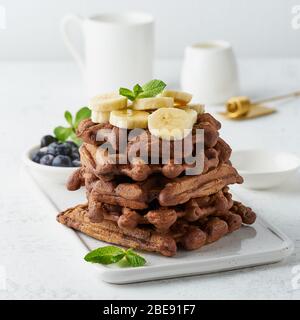 Gaufres à la banane au chocolat avec sirop d'érable sur table blanche, gros plan, vue latérale. Banque D'Images