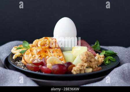 Superbe copieux petit déjeuner de pâques sur fond gris, avec plaque sombre. Service d'étage. Gaufres croustillantes avec confiture, œufs durs, pepperoni, fruits frais et maison Banque D'Images