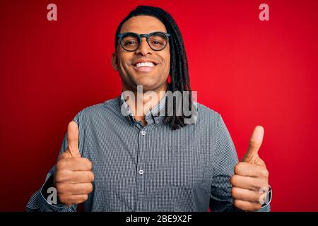Jeune homme africain avec des cadenas portant une chemise décontractée et des lunettes signe de succès faisant un geste positif avec la main, me fait sourire Banque D'Images