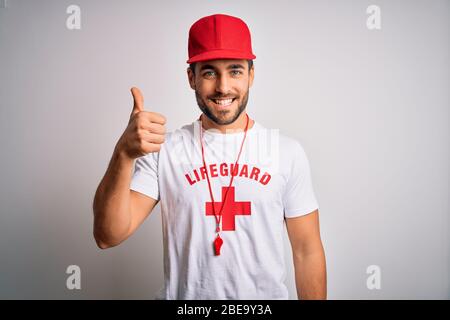 Jeune homme de maître de maître avec barbe portant un t-shirt avec croix rouge et siffler en faisant des pouces heureux vers le haut geste avec la main. Approbation de l'expression looki Banque D'Images