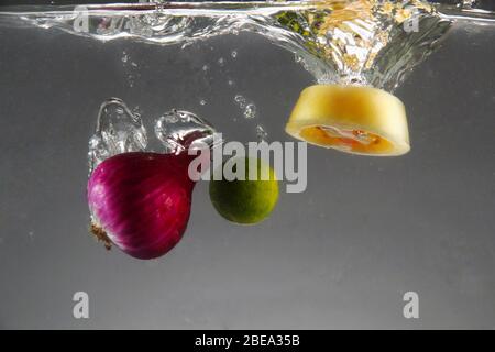 Photo de l'oignon rouge, de la tomate et du calamansi a chuté dans l'eau Banque D'Images