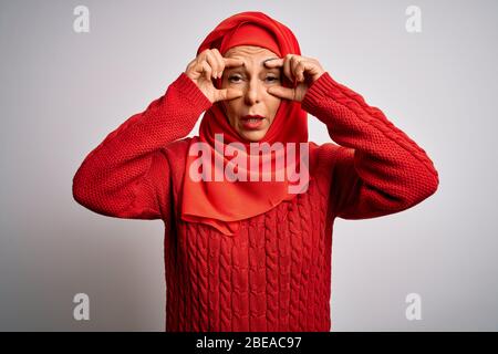 Femme brunette d'âge moyen portant un hijab traditionnel musulman sur fond blanc isolé essayant d'ouvrir les yeux avec les doigts, endormie et fatigué pour morni Banque D'Images