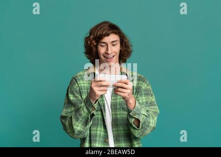 Restez à la maison. Jeune gars excité chat en ligne sur téléphone mobile, fond couleur Banque D'Images