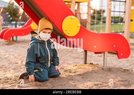 Un garçon dans un masque de protection joue dans le terrain de jeu pendant le coronavirus et la pandémie de Covid - 19 Banque D'Images