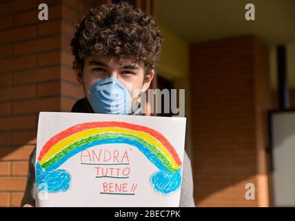 Turin,Piémont,Italie.Mars 2020.quarantaine de Cornonavirus.Portrait d'un garçon caucasien brun mauresque avec masque bleu et un dessin avec l'arc-en-ciel et le Banque D'Images