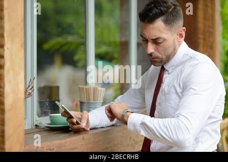 Portrait d'un homme d'affaires en attente et en train de vérifier son heure au café Banque D'Images