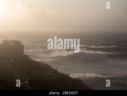 Vue sur Praia do Norte et le célèbre phare de Nazare tandis que les vagues s'écrasent au soleil couchant. Banque D'Images