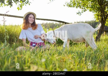 Humour, maison blanche ferme chèvre boutter une jeune fille adolescente. Paysage de coucher de soleil pittoresque en été Banque D'Images