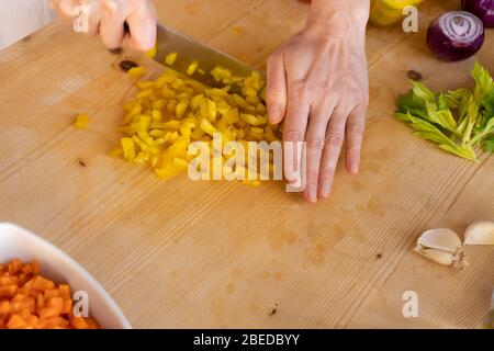 Moments de vie quotidienne dans la cuisine méditerranéenne: Vue à bas angle d'une jeune femelle cuisinier couper un poivre jaune avec divers légumes autour de lui Banque D'Images