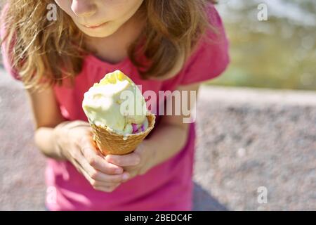 Tasse à cône gaufré avec crème glacée jaune dans la main de la fille d'enfant. L'été, la glace fondante Banque D'Images