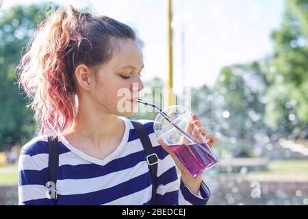 Une jeune fille tenant le verre avec de la paille avec une boisson violette dans la main. Une soif de désaltérage féminine le jour ensoleillé de l'été, fond du ciel, espace de copie Banque D'Images