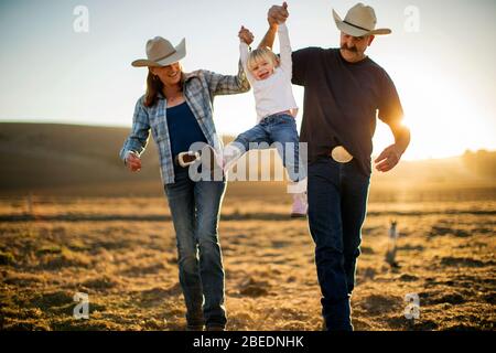 Couple mûr balançant leur fille entre eux sur leur ranch au coucher du soleil Banque D'Images