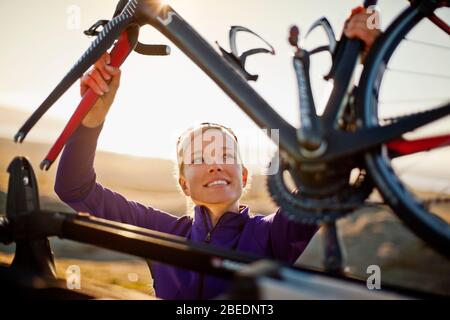 Jeune femme souriante qui fixe son vélo à la galerie de toit de sa voiture Banque D'Images