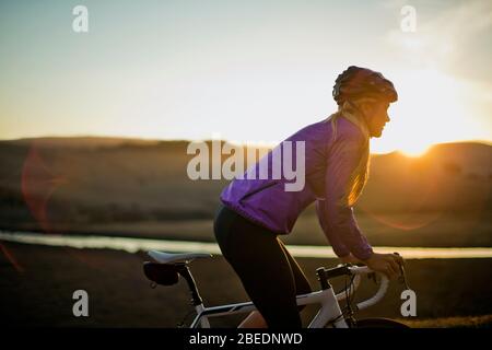 Jeune femme qui descend sur une route de campagne au coucher du soleil Banque D'Images