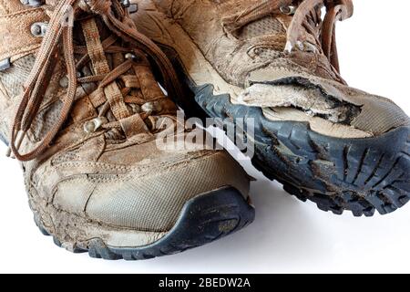 Une paire de chaussures de randonnée usées, fendues et boueuses sur un fond blanc Banque D'Images