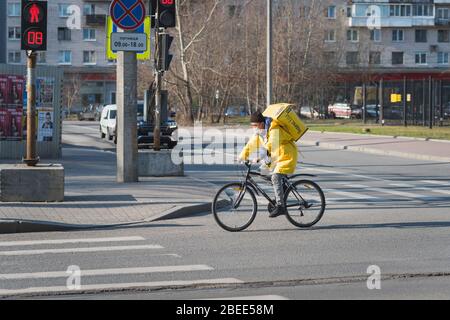 Saint-Pétersbourg, Russie - 7 avril 2020: Un cycliste en uniforme jaune porte une boîte par le service de livraison de nourriture de restaurant 'Yandex EDA'. Banque D'Images