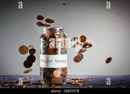 Pièces de monnaie tombant sur un pot de monnaie de poche plein de Sterling britannique Banque D'Images