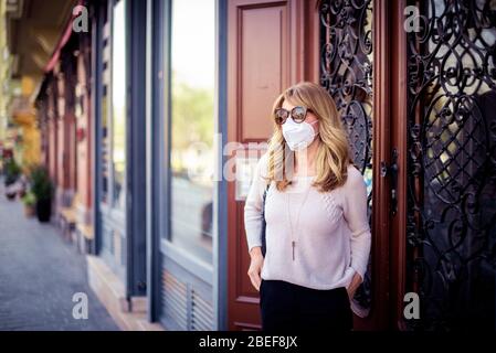 Portrait de la femme d'âge moyen portant un masque facial en se tenant dans la rue pendant l'éclosion de coronavirus. Banque D'Images