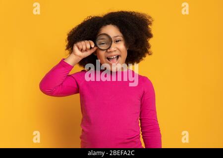 Belle petite fille africaine regardant par la loupe sur fond jaune Banque D'Images