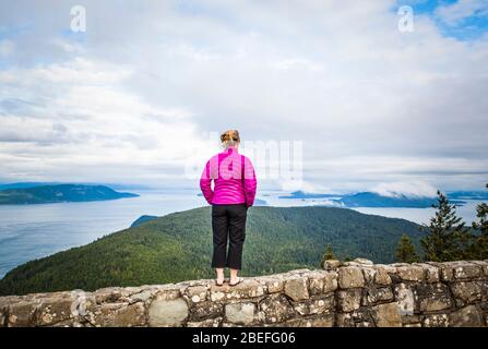 Une femme debout au sommet d'un mur de roche au sommet du mont Constitution dans le parc national de Moran, Orcas Island, Washington, États-Unis. Banque D'Images