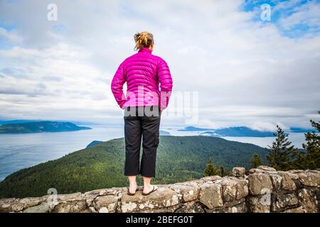 Une femme debout au sommet d'un mur de roche au sommet du mont Constitution dans le parc national de Moran, Orcas Island, Washington, États-Unis. Banque D'Images