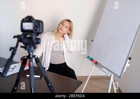 Une jeune femme enceinte tuteur enregistre les cours de vidéo de formation à la caméra, elle se tient debout et montre avec un stylo sur un tableau de conférence avec des graphiques et des diagrammes Banque D'Images