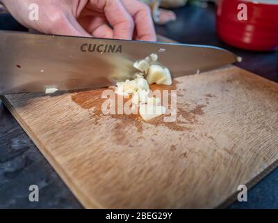 Gousse d'ail à trancher à la main humaine (Allium sativum) avec un couteau de cuisine tranchant sur un tableau de découpe en bois, avec un foyer sélectif Banque D'Images