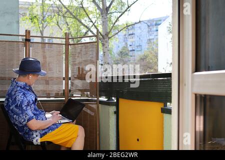 homme sur le balcon de sa maison, un gars dans un chapeau, travail à distance sur l'ordinateur Banque D'Images