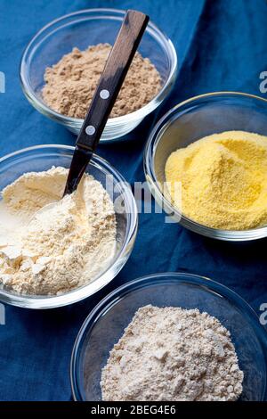 Divers légumes farine sans gluten maïs, sésame, avoine, noix de coco dans un bol en verre sur fond textile bleu gros plan.alternative à la farine de blé Banque D'Images