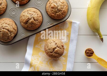 Muffins aux noix de banane dans un plateau de muffin avec banane, cannelle et serviette de cuisine sur fond de bois blanc Banque D'Images