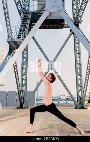 Jeune sportif exécutant des mouvements articulaires de yoga dans une zone urbaine de la ville. Banque D'Images