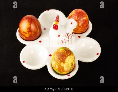 Support d'œufs en porcelaine blanche avec trois œufs de Pâques isolés sur fond noir Banque D'Images