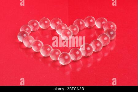 Billes de verre en cristal assemblées en forme de coeur sur le fond rouge Banque D'Images