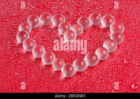 Billes de verre en cristal assemblées en forme de coeur sur le fond rouge Banque D'Images