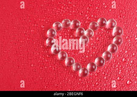 Billes de verre en cristal assemblées en forme de coeur sur le fond rouge Banque D'Images