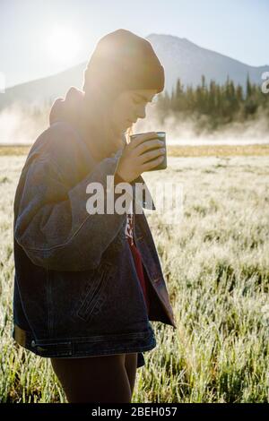 Image verticale de la jeune femme tenant une tasse réutilisable au lever du soleil Banque D'Images