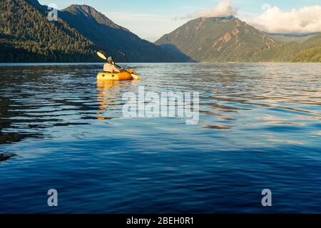 Jeune homme pagayant sur le lac vers la montagne au coucher du soleil Banque D'Images