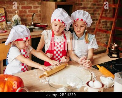 Trois petits chefs qui apprécient dans la cuisine font des gâteaux. Filles dans la cuisine. Ménage en famille. Banque D'Images