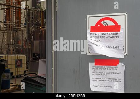 Ferndale, Michigan, États-Unis. 13 avril 2020. Un panneau sur la porte de Valentine Distiling Co. Exige que les visiteurs portent des masques et pratiquent la distanciation sociale. La distillerie a arrêté sa production de bourbon, de gin et de vodka, ne faisant que de l'aseptisant pour les mains en raison de la pandémie de coronavirus. Crédit: Jim West/Alay Live News Banque D'Images