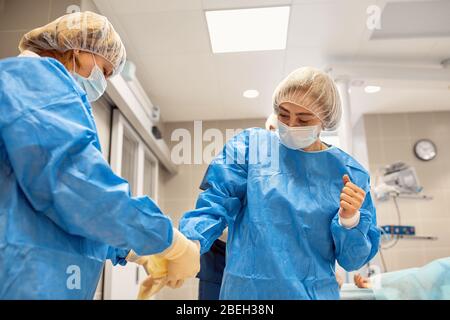 Assistant de salle d'opération aidant le chirurgien en mettant des vêtements stériles. Vous pouvez les voir en profil en mettant leurs bottes chirurgicales. Banque D'Images